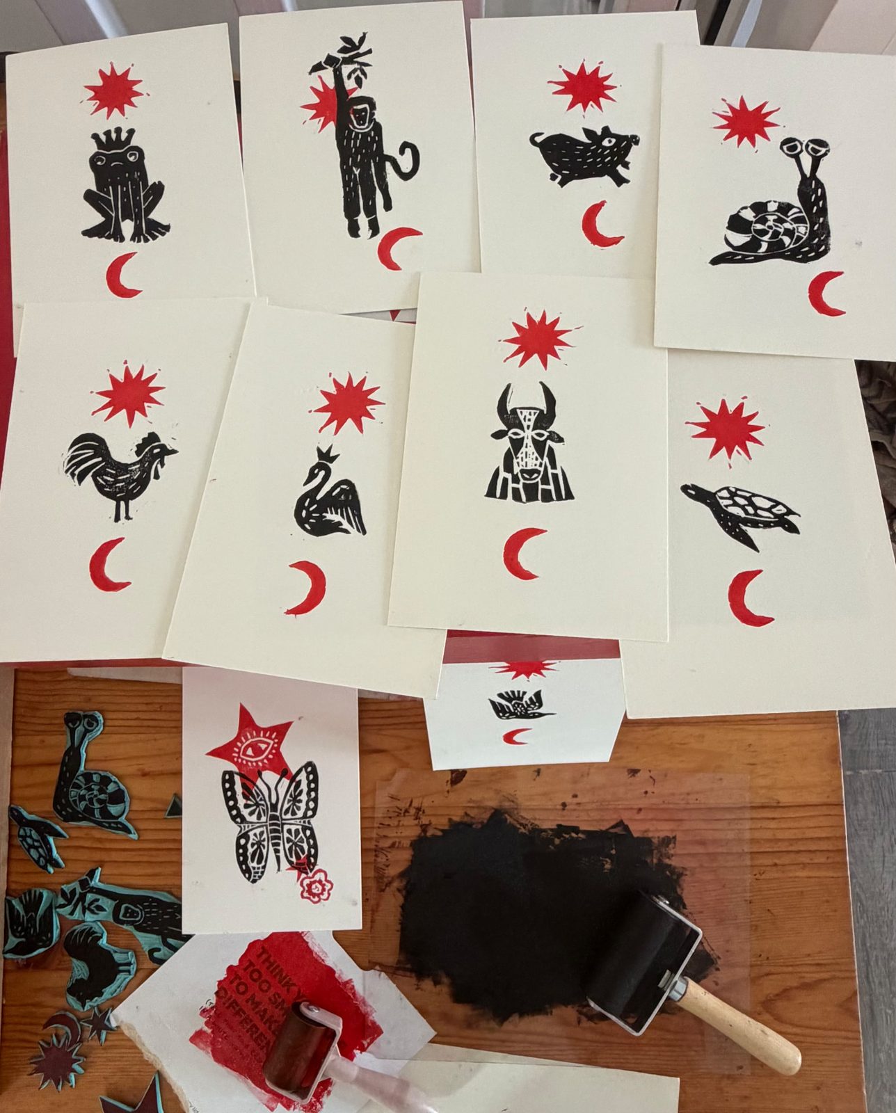 Hand-printed animal lino cards with red stars and moons, laid out on the studio table