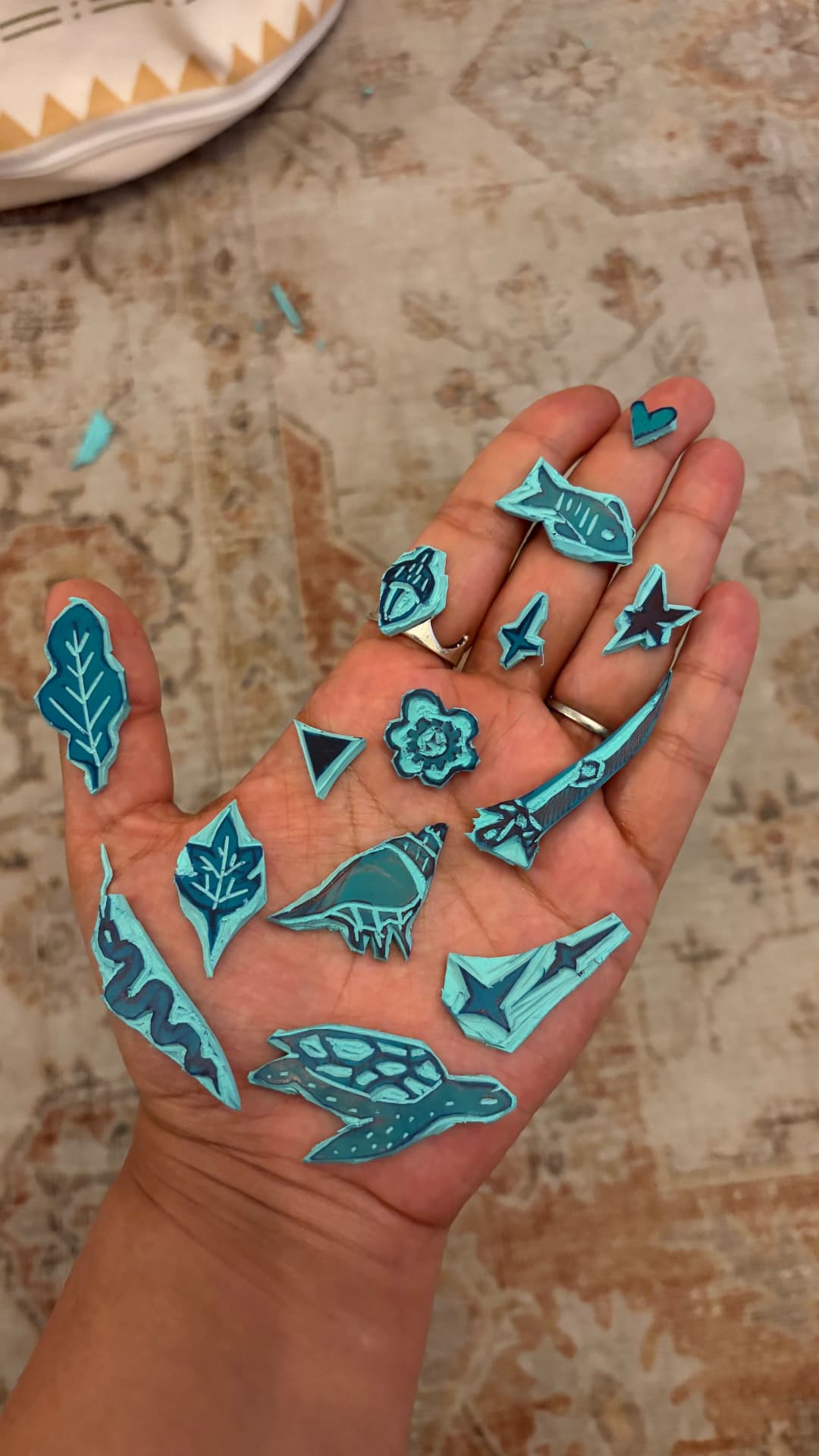 A hand holding many small hand-carved lino stamps