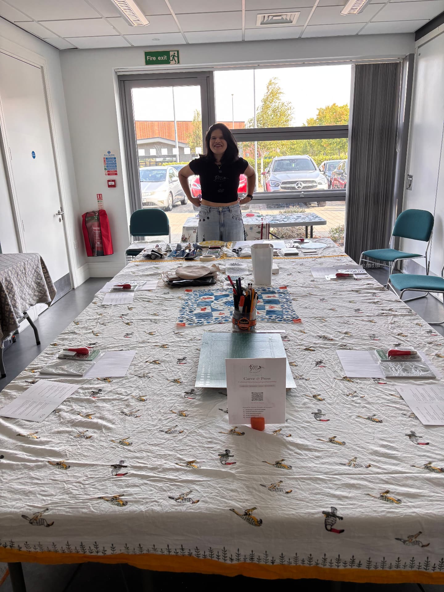 Aparna behind a long workshop table laid with carving tools and a Carve & Press sign